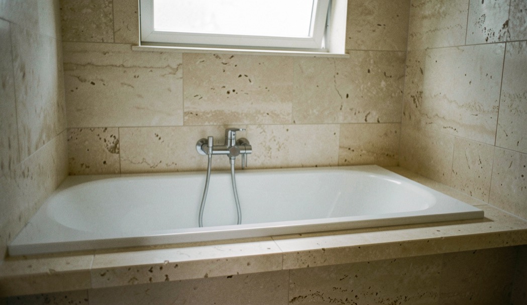 Piano di lavoro in marmo bianco venato in una cucina compatta, luce calda di una applique laterale, inquadratura ravvicinata di tre quarti con piante in vaso sul davanzale della finestra sullo sfondo.